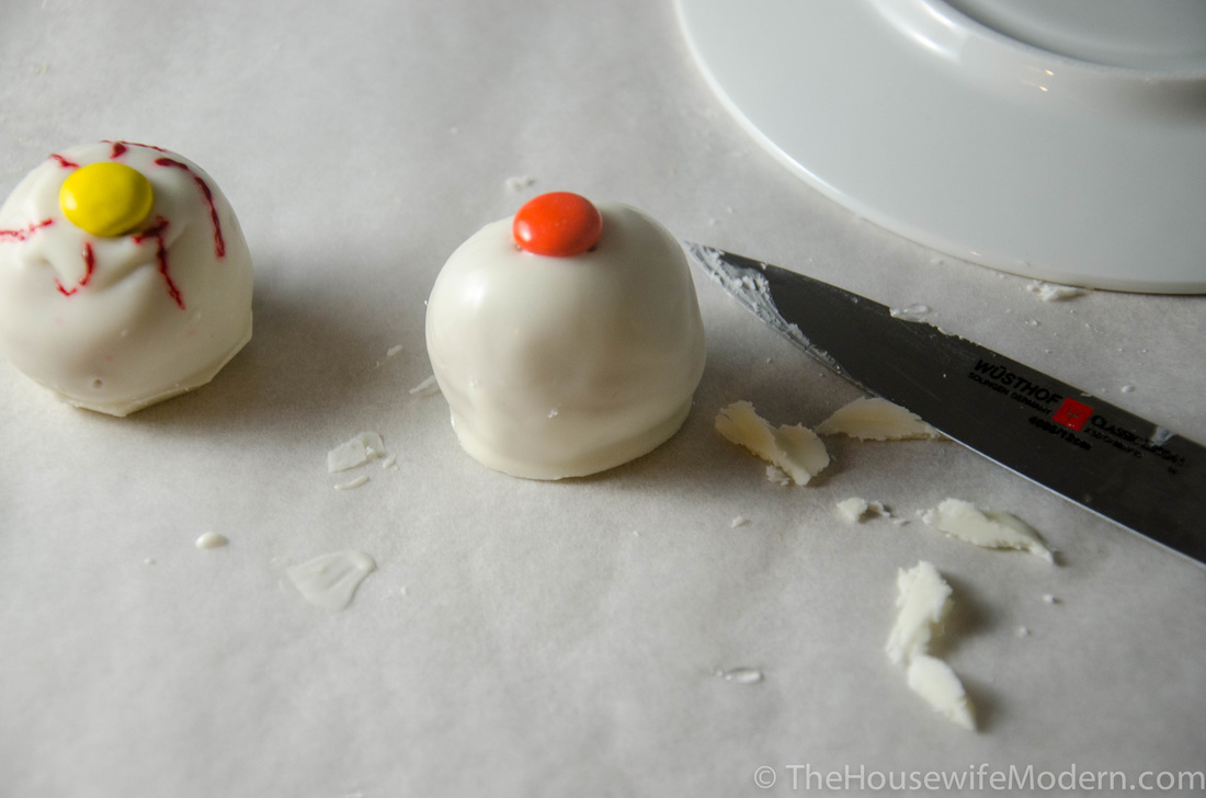 Drizzle a *tiny* bit of chocolate onto top. Gently push an M&M into top. After it has hardened, trim off any excess chocolate around the bottom.