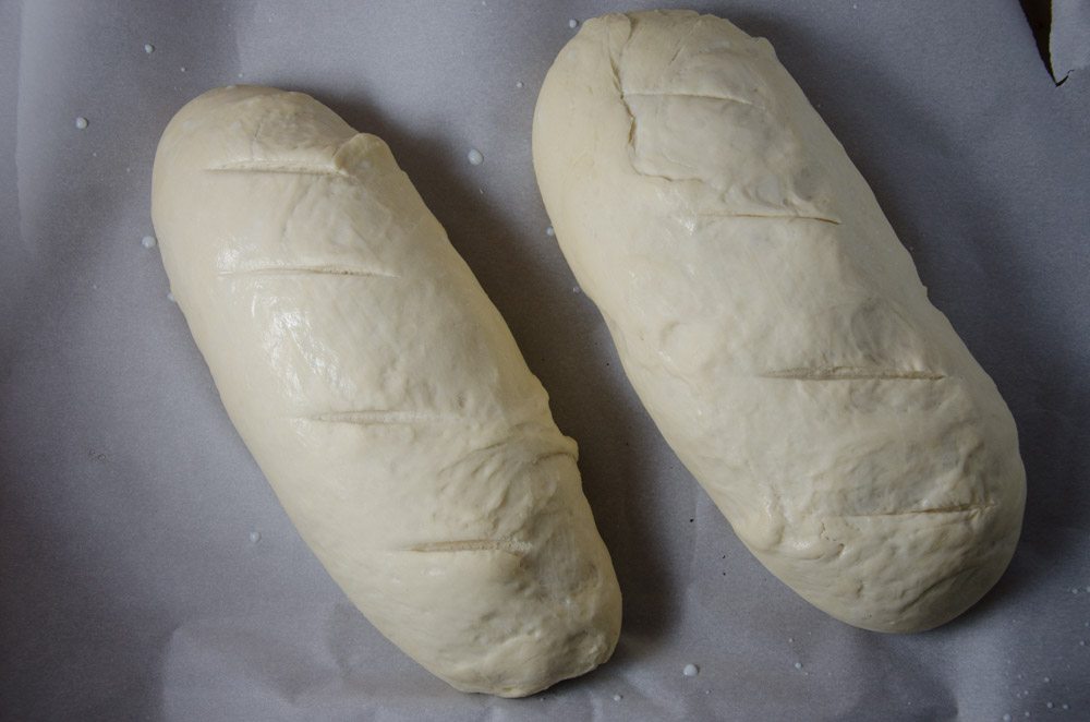 Normally, place loaves onto large baking sheet that has a tiny bit of cornmeal sprinkled across the surface. Allow to rise 30 minutes. (This pic has them on parchment paper...I was testing various loaves.) When dough is risen, carefully brush milk on the top of the loaves. With a sharp knife, make 3-4 shallow diagonal slashes across the top of the loaf. (This allows some steam to escape so it expands evenly during the baking process).