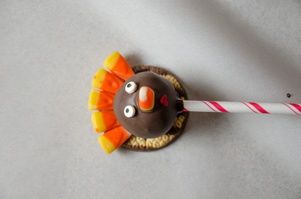 LR_Turkey Cake Pops_step3 prep-6 While chocolate is still wet, place candy corn on for nose. Use heart-shaped sprinkle, upside down, for mouth. Add candy eyes. If chocolate hardens too much, use a small amount of wet chocolate on the back of mouth/eyes to get it to stick.