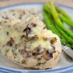 Gouda and mushroom stuffed chicken with wild rice and asparagus on pottery plate.