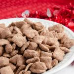 Image of peanut butter brownie puppy chow in white bowl with red cloth and white marble underneath.