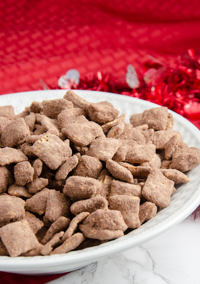 Image of peanut butter brownie puppy chow in white bowl with red cloth and white marble underneath.