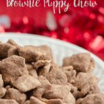 Pin mage of peanut butter brownie puppy chow in white bowl with red cloth behind it.. White text overlay.