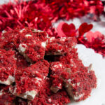 Vertical image for red velvet bark. Close-up of bark piled on white plate with red tinsel in background
