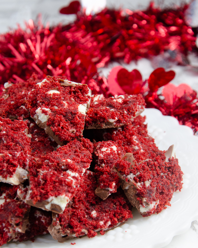 Vertical image for red velvet bark. Close-up of bark piled on white plate with red tinsel in background