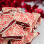 Vertical image for red velvet bark. Close-up of bark piled on white plate with red tinsel in background