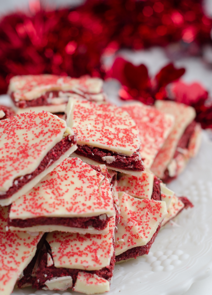 Vertical image for red velvet bark. Close-up of bark piled on white plate with red tinsel in background