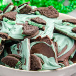 White bowl with mint oreo bark. White marble background with green tinsel.