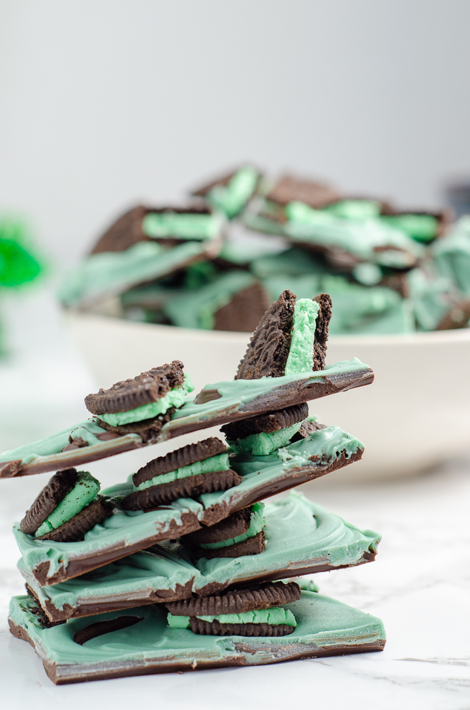 Stack of 4 pieces of mint oreo bark with bowl in background. On white marble countertop.