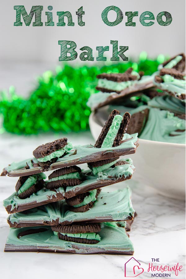Pin image for mint oreo bark. Stack of mint oreo bark in foreground. White bowl full of mint oreo bark with green tinsel in background.