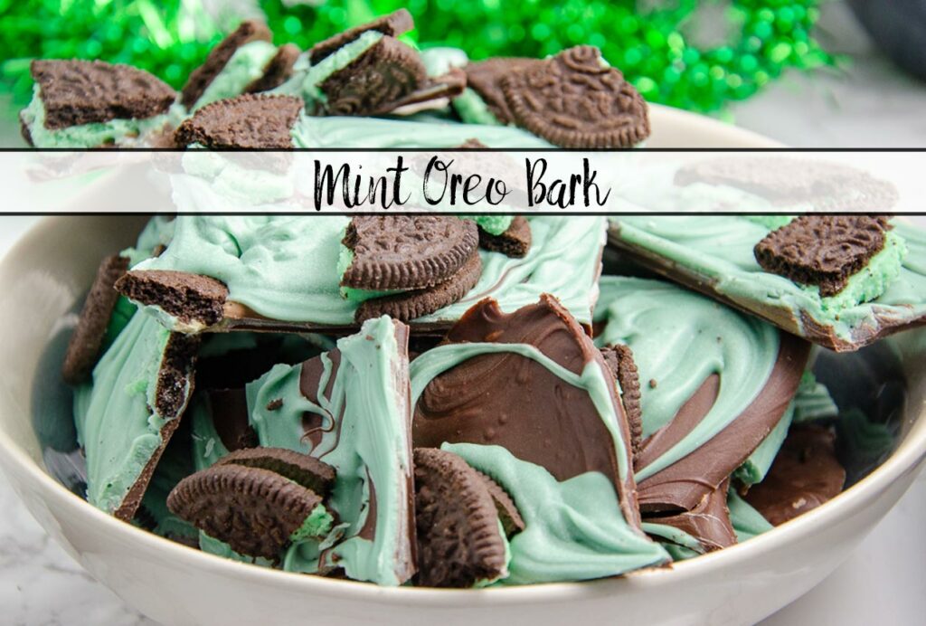 Featured image for mint oreo bark. White bowl full of mint oreo bark with green tinsel in background.