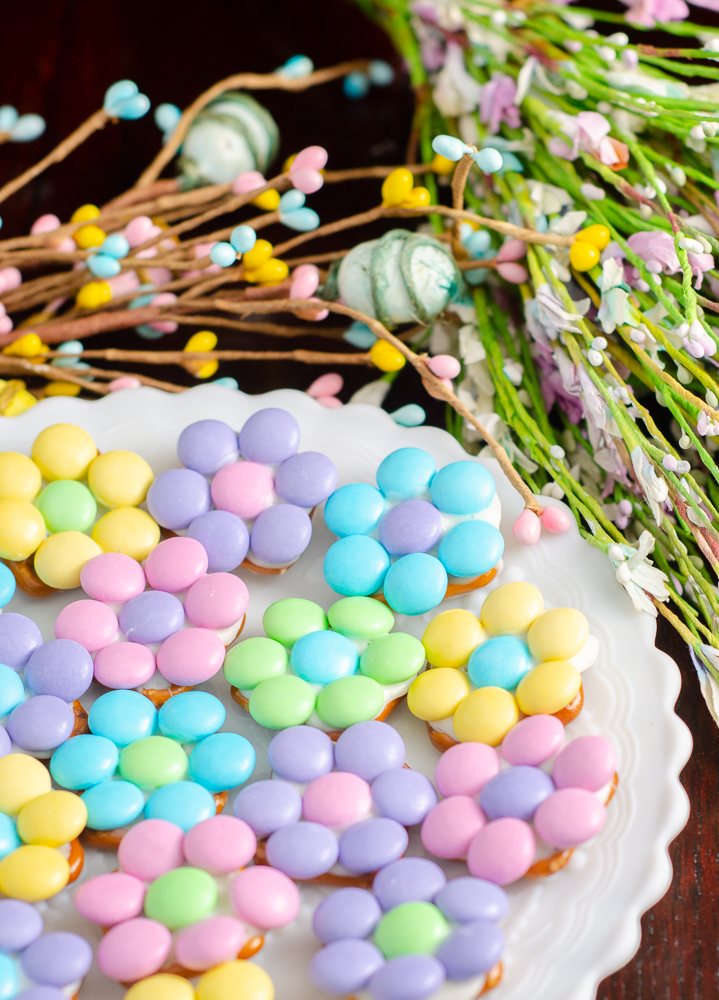 Spring flower pretzel bites on white plate with egg & flower foliage.