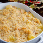 White deep oval casserole dish full of cheesy ham and potato casserole. Fall wire wreath in background.
