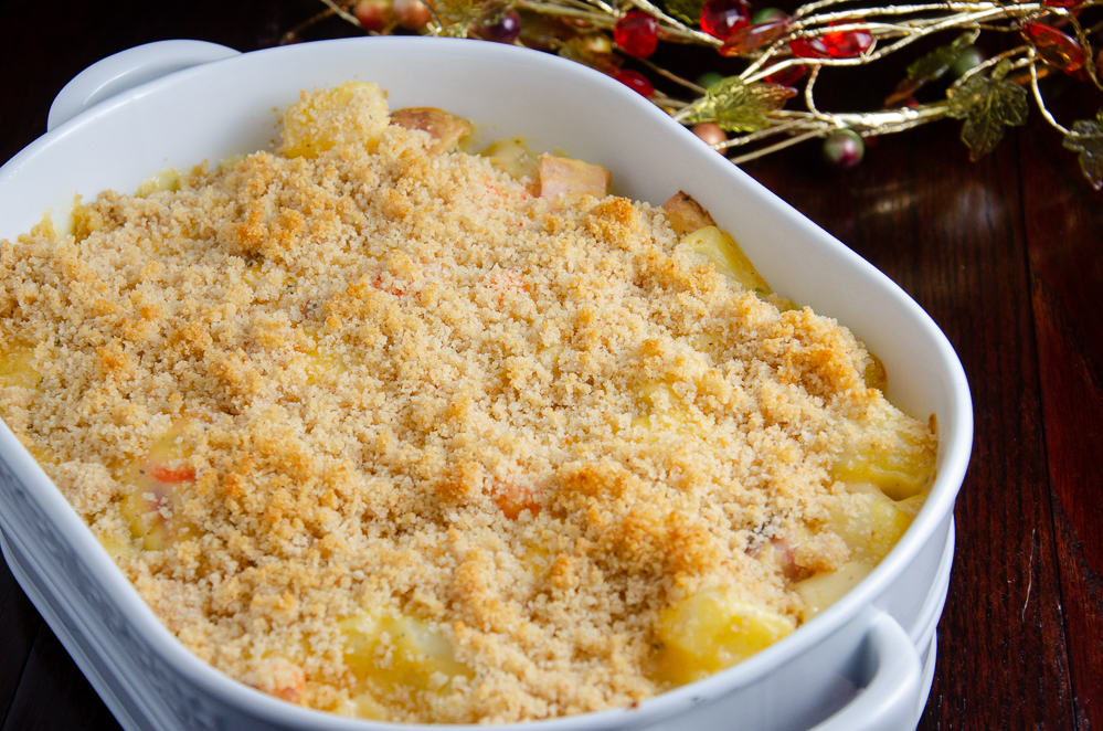 White deep oval casserole dish full of cheesy ham and potato casserole. Fall wire wreath in background.