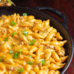 Homemade hamburger helper in cast-iron skillet on wood planks. Cheeseburger macaroni version.