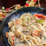 Chicken fettuccine with roasted vegetables in cream sauce in a blue bowl. Wood in background.