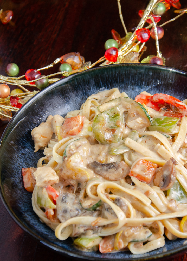 Chicken fettuccine with roasted vegetables in cream sauce in a blue bowl. Wood in background.