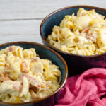 Two dark blue stoneware bowls of casserole with red cheesecloth on side. Horizontal image.