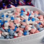 Patriotic muddy buddies in white oval dish with sparkle wreath in background.