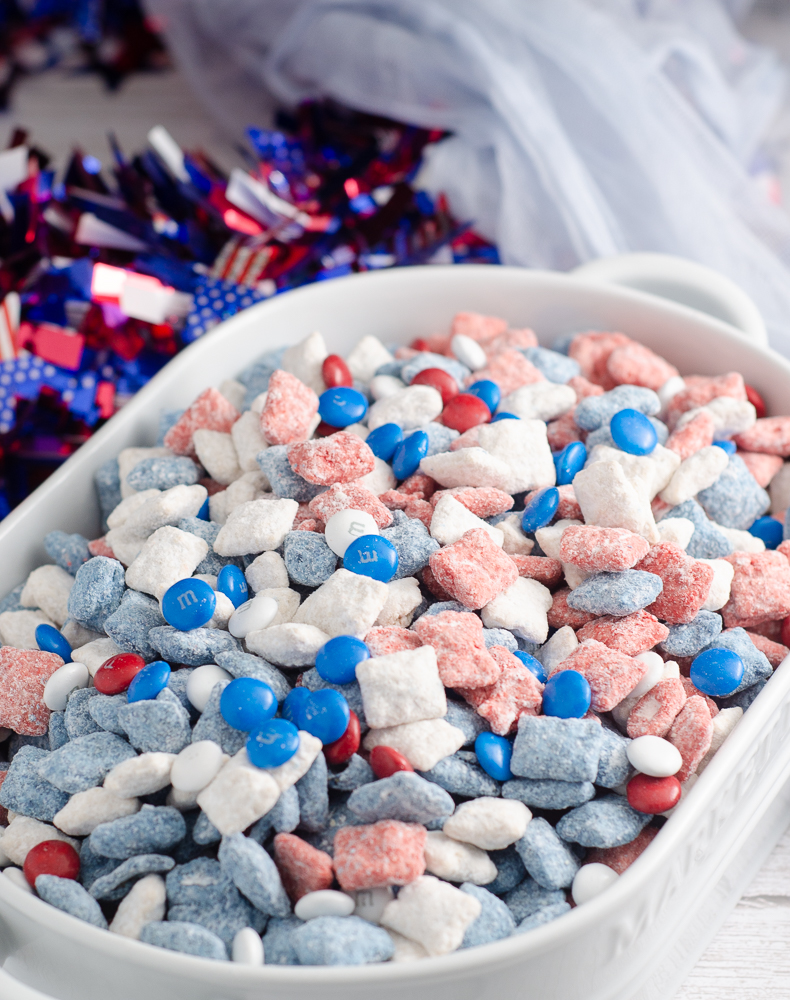 Patriotic muddy buddies in white oval dish with sparkle wreath in background.