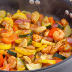 Shrimp and vegetable skillet in large black skillet. White wood under pan.