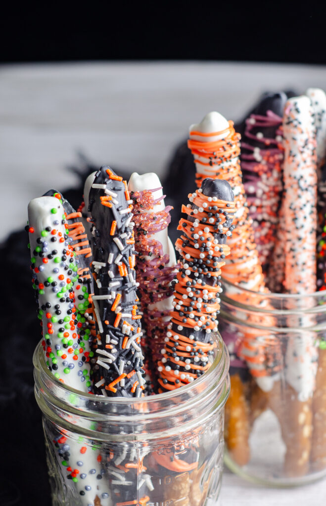 Halloween pretzel rods displayed in mason jars for a fun Halloween party centerpiece. These colorful chocolate covered pretzels make easy party treats, classroom snacks, and edible Halloween gifts.