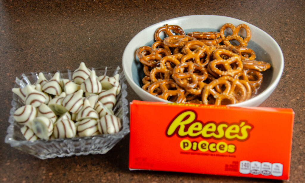 Pretzels, striped Hershey's Kisses, and Reese's Pieces prepped before baking.
