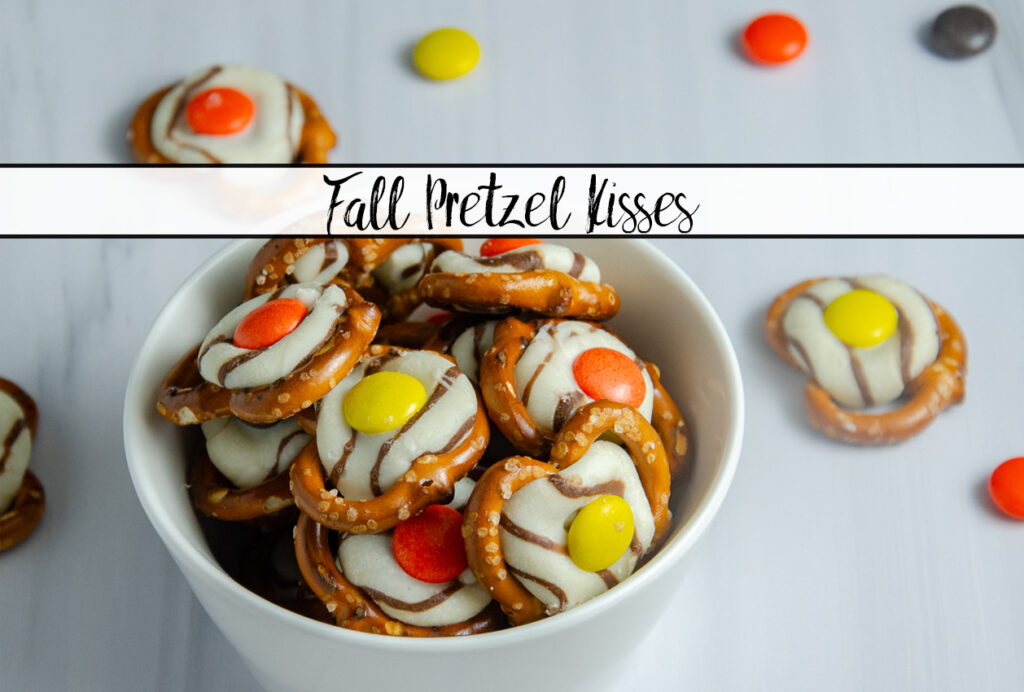 Featured image for fall pretzel kisses. Prepared pretzels in a small white bowl on white background with a few pretzels and Reese's Pieces scattered around them.