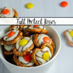 Featured image for fall pretzel kisses. Prepared pretzels in a small white bowl on white background with a few pretzels and Reese's Pieces scattered around them.