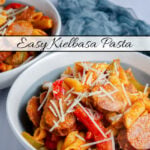 Polska kielbasa, penne pasta, bell peppers, and onion with a red sauce. Dished up in two white and grayish blue bowls on a white and gray background with light blue cheesecloth. Text overlay.